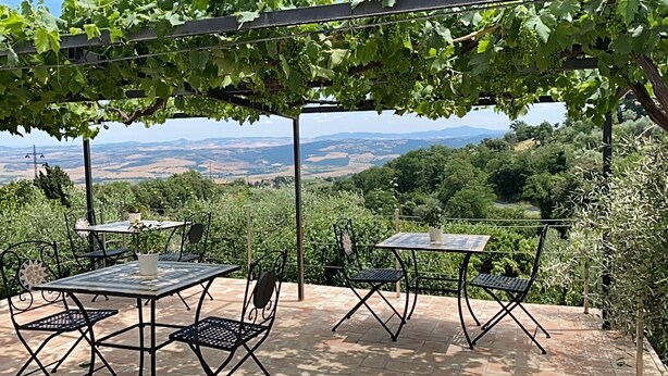 Eine Terrassengruppe mit Tischen und Stühlen, umgeben von viel Grün und Blick auf ferne Hügel.