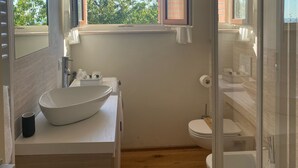 Ein modernes Badezimmer mit großem Fenster, einem weißen Waschbecken und einer Duschkabine aus Glas.