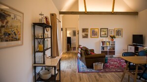 Un salon chaleureux avec un plancher en bois, un canapé, une table basse et une bibliothèque. On y trouve un téléviseur posé sur un meuble et une fenêtre avec des rideaux.