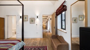 Une chambre avec un grand lit, un coin salon avec un banc, un miroir et des tableaux encadrés aux murs.