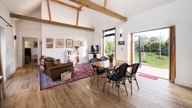 Un salon spacieux doté d’un parquet, d’un canapé en cuir marron, d’une table à manger avec des chaises et d’une grande fenêtre donnant sur le jardin.