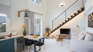 Una cocina moderna con comedor, una escalera y una sala de estar con sofá y televisor.