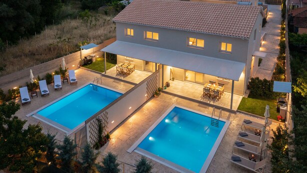 Una casa de dos pisos con piscina, mobiliario exterior y un porche cubierto.