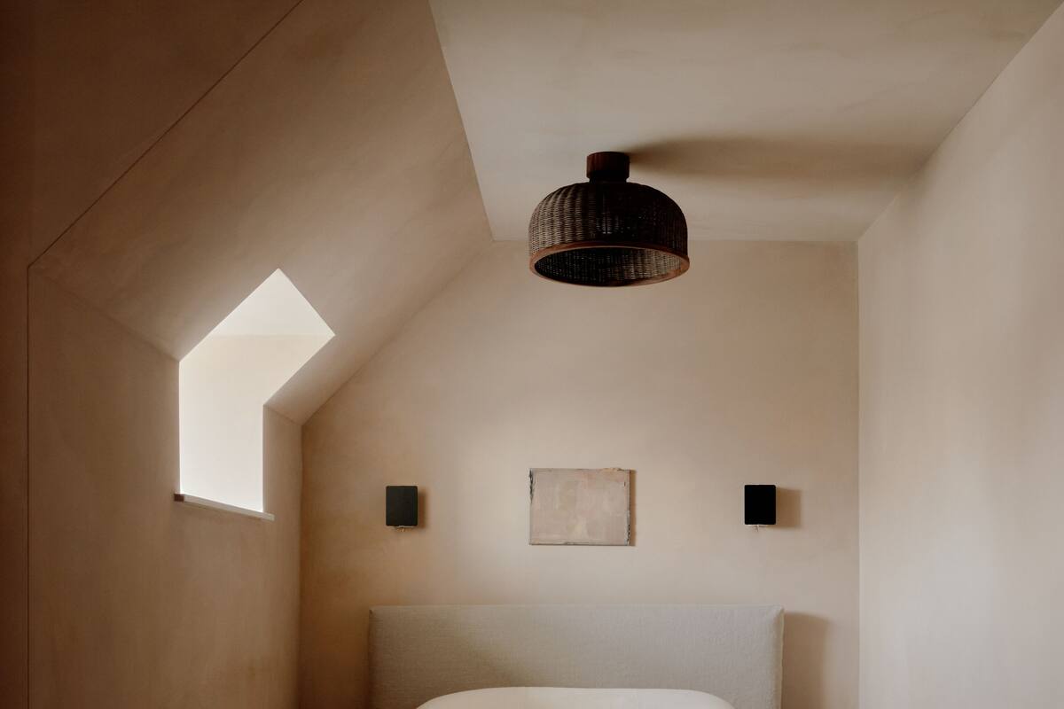 Een slaapkamer met een schuine kap, een enkel bed, een klein raam en een hanglamp.