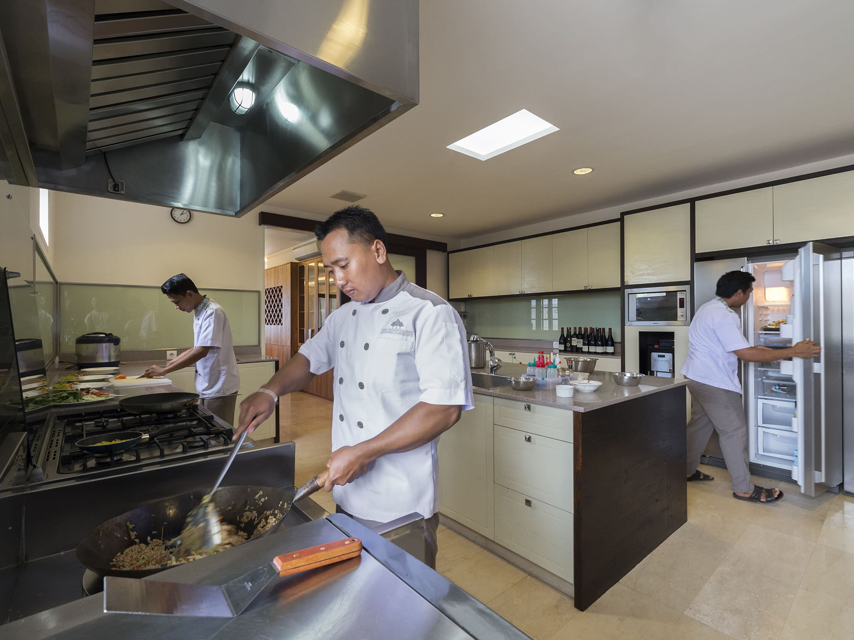 A modern kitchen with stainless steel appliances, a large island, and a professional chef preparing food.