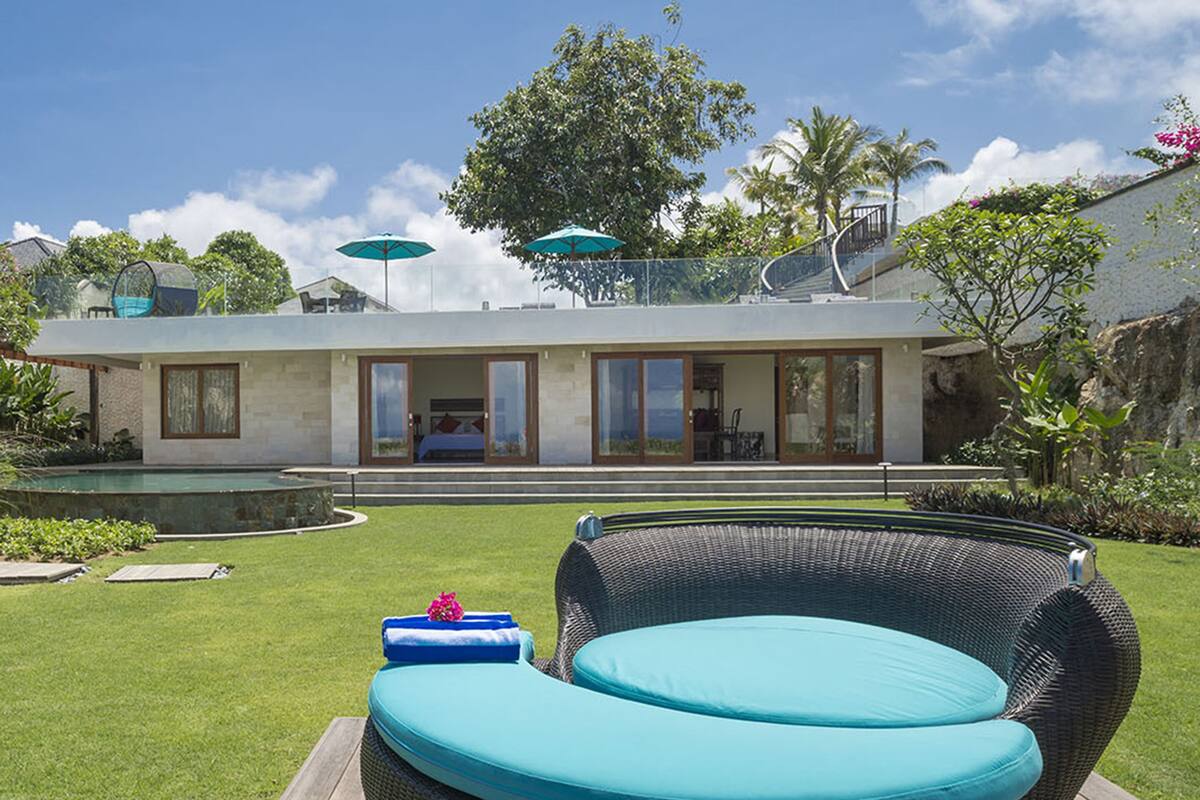 Une maison moderne dotée d’une piscine, d’un patio couvert avec des chaises et d’un grand arbre dans le jardin.
