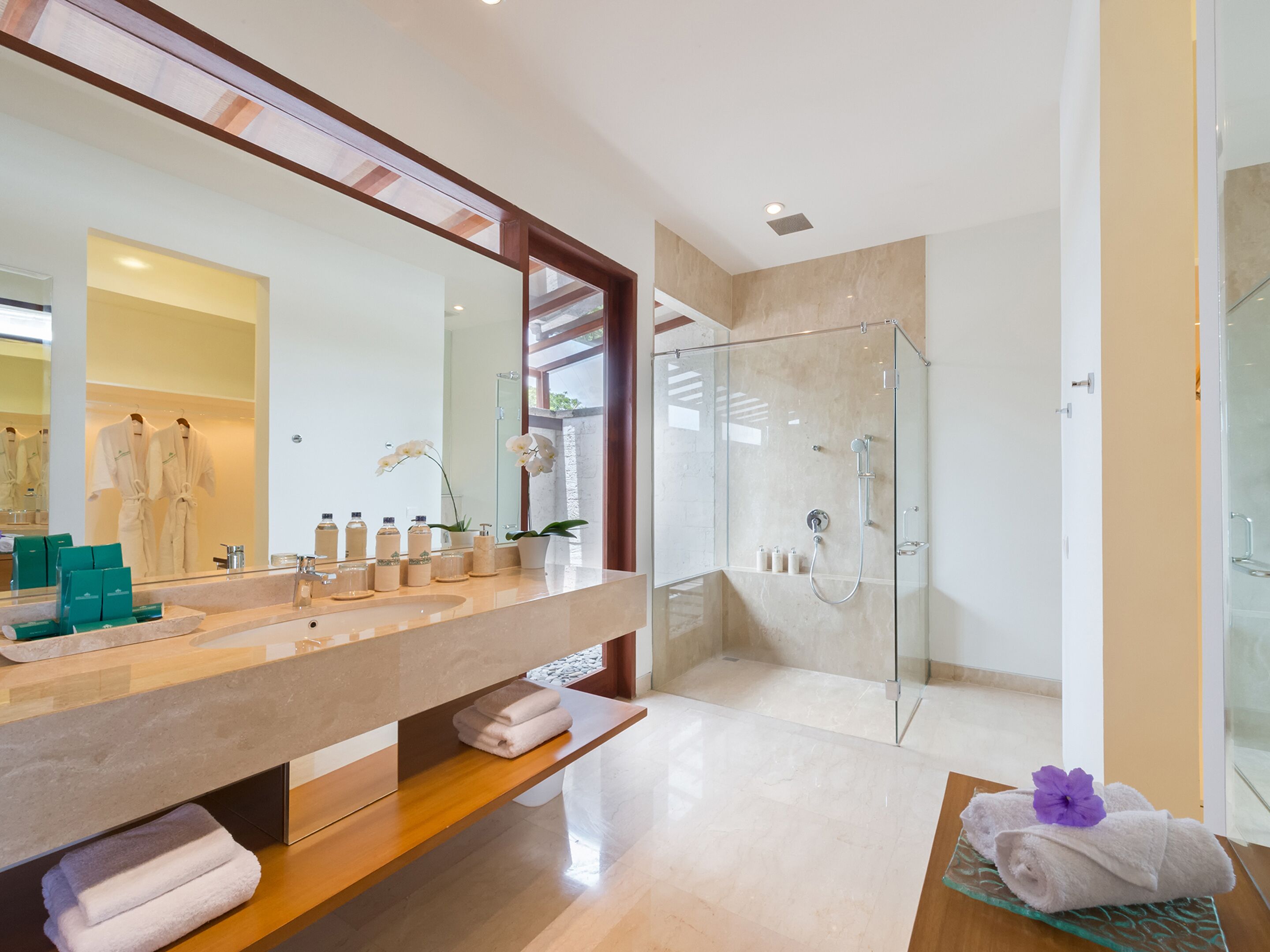 A modern bathroom with a large mirror, a glass shower enclosure, and a vanity with a beige countertop.