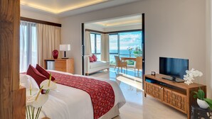 A modern hotel room with a large bed, a TV, a balcony with a view of the sea, and a dining area. - Pandawa Cliff Estate (Kutuh)