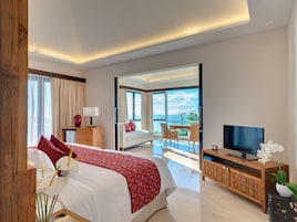 A modern hotel room with a large bed, a TV, a balcony with a view of the sea, and a dining area.