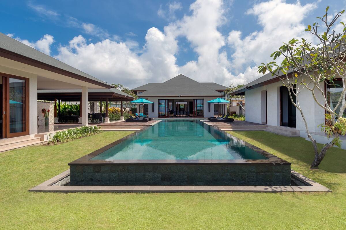 Une maison moderne dotée d’une piscine, d’un patio couvert et d’un jardin luxuriant.