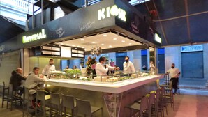 Un espace de restauration avec un îlot central où les plats sont servis, entouré de tables et de chaises.