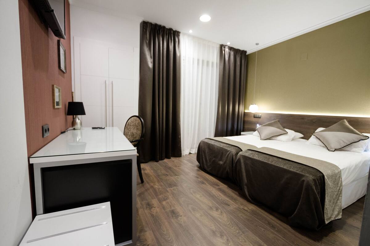 A hotel room with a bed, bedside tables, a desk, a chair, and a lamp.