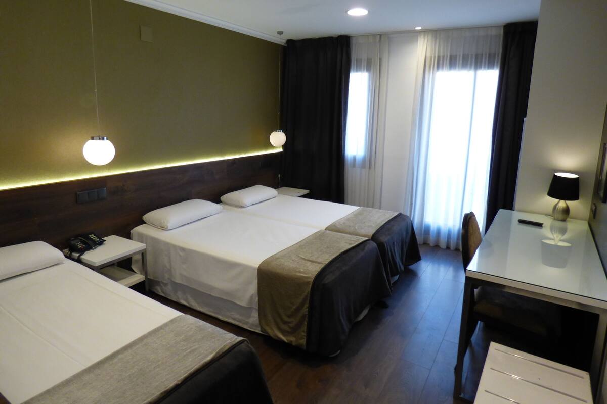 A hotel room with two beds, a desk, a chair, a telephone, and a lamp.