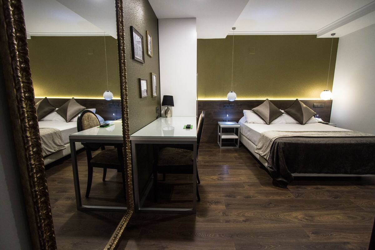 A hotel room with two beds, a desk, and a chair. There are bedside tables with lamps.