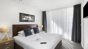 Une chambre d’hôtel avec un grand lit, deux tables de chevet avec des lampes, un tableau encadré au mur et une fenêtre avec des rideaux.