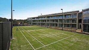 Un court de tennis jouxtant un bâtiment moderne doté de grandes fenêtres et d’un toit plat.