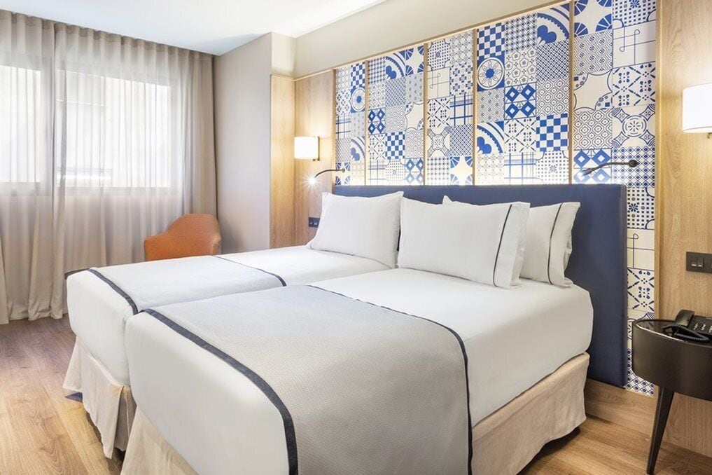 Una camera d'albergo con due letti, una testiera in legno, una parete decorata e una scrivania con il telefono e una sedia.