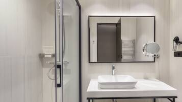 Un baño moderno con cabina de ducha de vidrio, un lavabo blanco y un espejo grande.