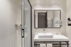 Un baño moderno con cabina de ducha de vidrio, un lavabo blanco y un espejo grande.