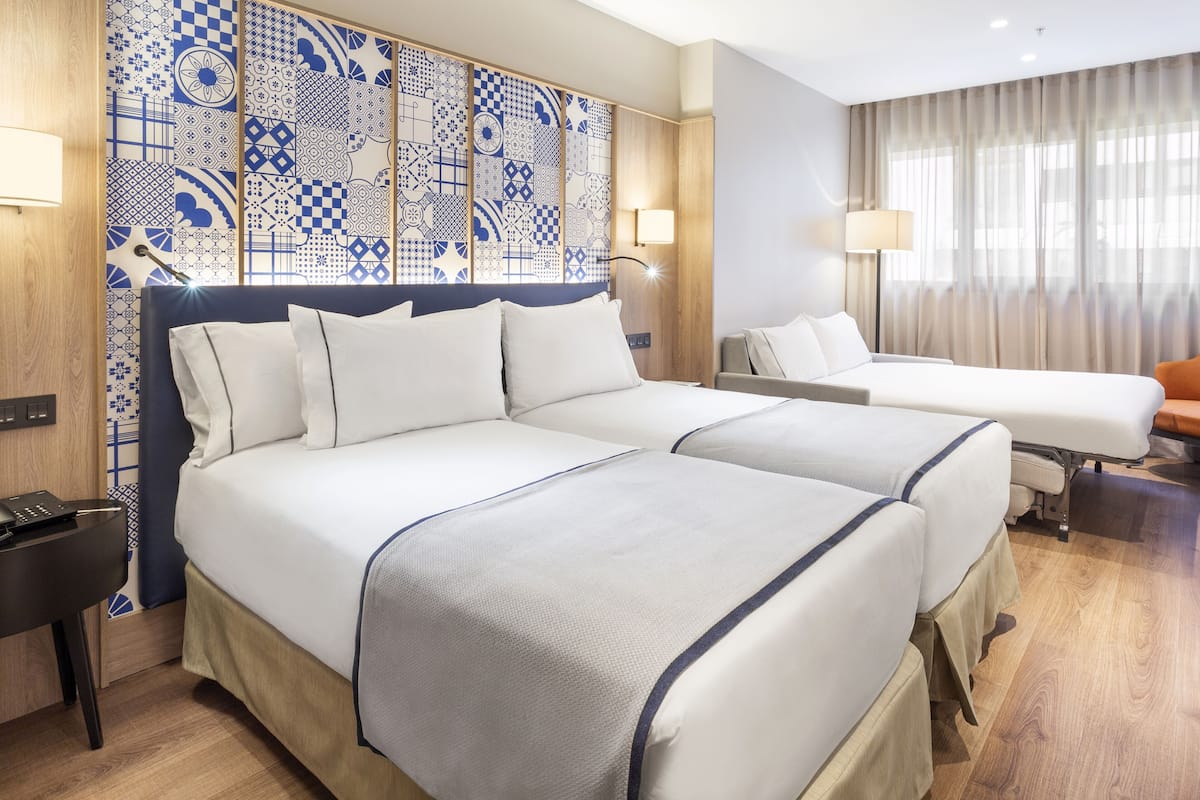 Hotellihuone, jossa on kaksi sänkyä, kuviollinen sängynpääty, työpöytä ja lamppu.