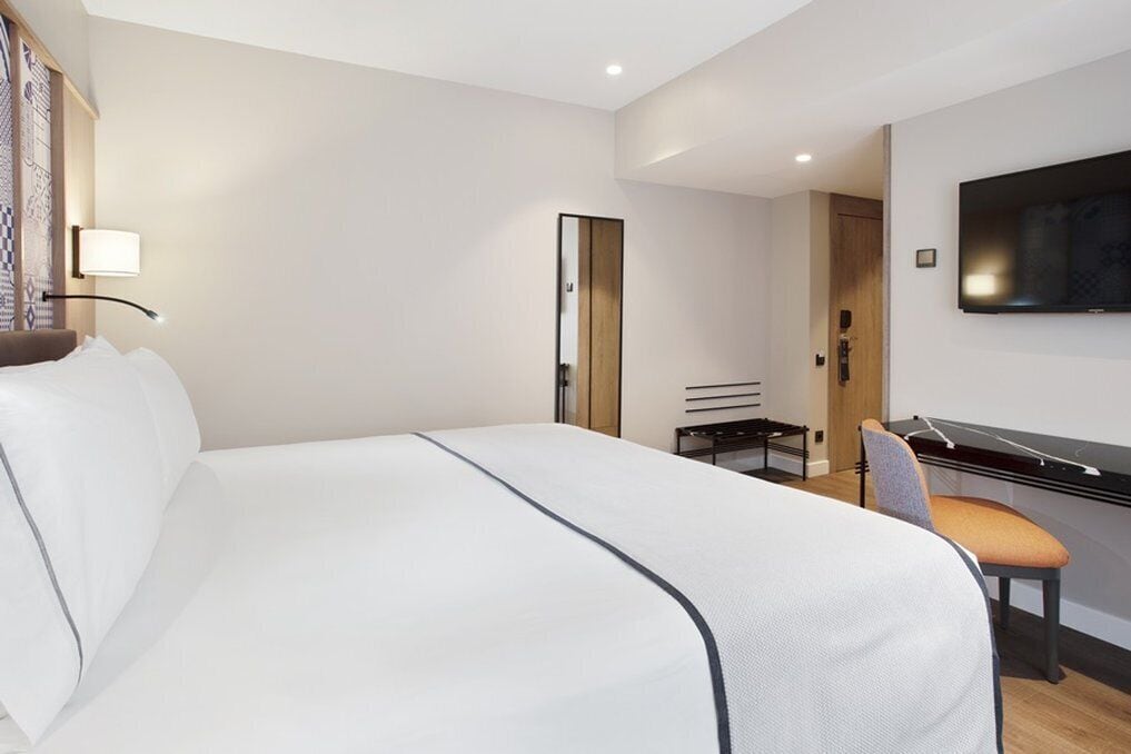 Habitación de hotel moderna con una cama grande, un escritorio con una silla, un televisor de pantalla plana y un espejo.