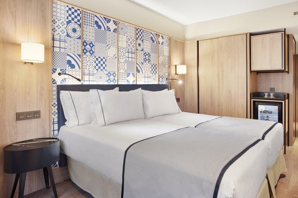 Una habitación de hotel con una cama grande, una mesita de noche, un televisor montado en la pared y un armario de madera.