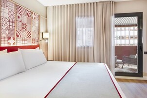 A hotel room with a large bed, a sliding glass door to a balcony, and a decorative wall panel.