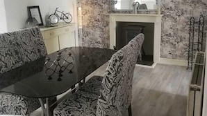 A dining area with a black table and patterned chairs, a bicycle, and a fireplace. - Tranquil Retreat - 3 Bedroom House With hot tub (Torquay)