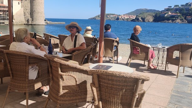 Un cafè a la vora del mar amb mobiliari de vimetes i vista al mar i edificis.