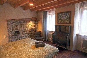 A rustic room with a stone fireplace, a bed with a patterned bedspread, a chair, and a vintage cabinet.