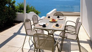 En overdækket terrasse med bord og stole, med udsigt over kysten.