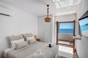 Une chambre à coucher comprenant un lit, une télévision, une fenêtre donnant sur la mer et une porte menant à un espace extérieur.