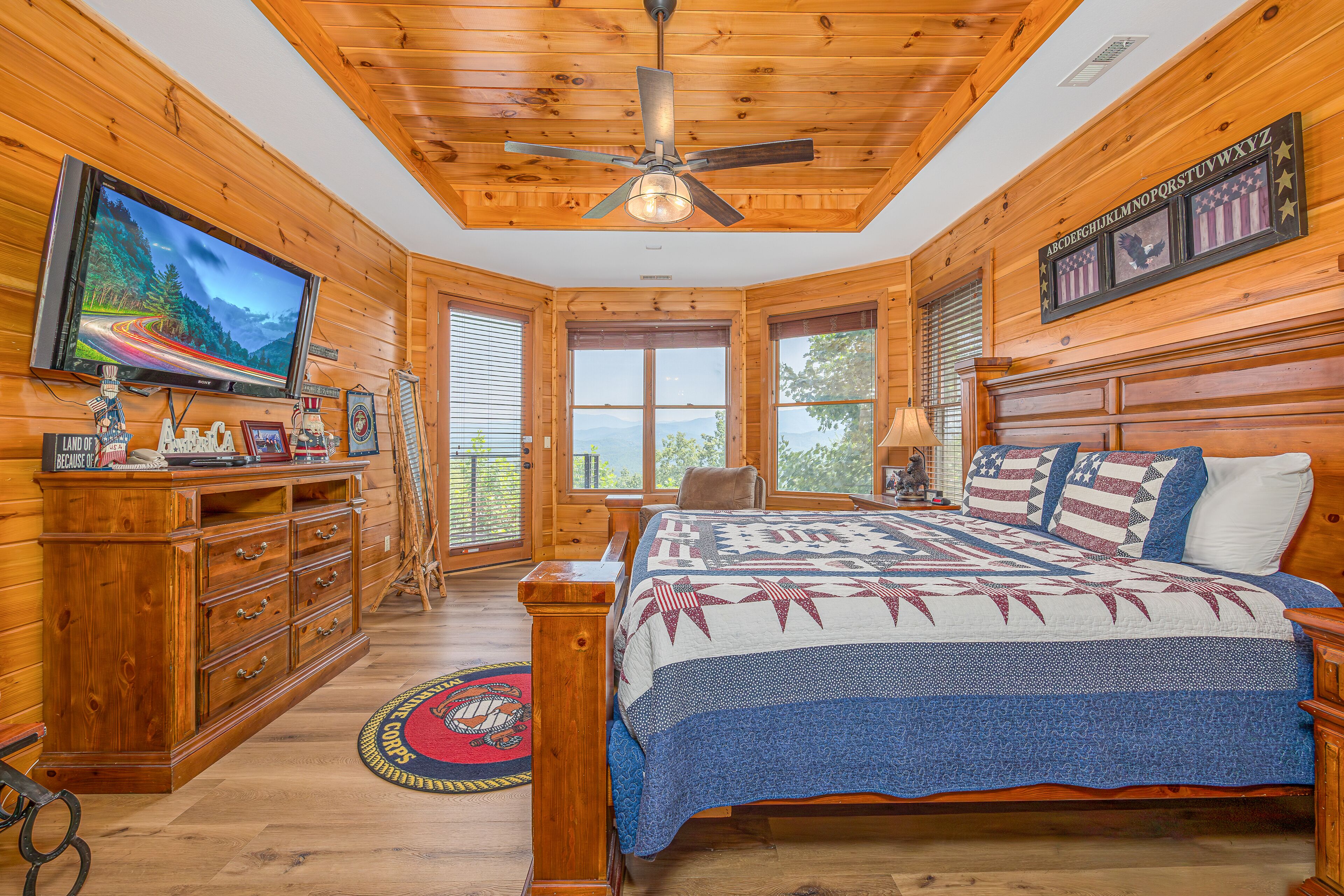 A wooden cabin bedroom with a bed, dresser, television, and a ceiling fan.
