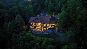 A large, multi-story house surrounded by dense forest, featuring a prominent outdoor deck and a visible swimming pool. - Five Bears Mountain View Lodge - Private Mtn Views -  Ultimate Luxury Cabin (Sevierville)