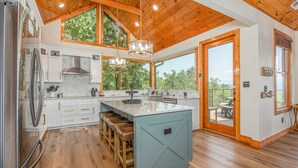A spacious kitchen with wooden beams, a large island with stools, and a view to the outdoors. - Five Bears Mountain View Lodge - Private Mtn Views -  Ultimate Luxury Cabin (Sevierville)