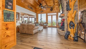 A lodge interior with wooden walls, a ceiling fan, a large wooden tree sculpture, and a view of mountains through large windows. - Five Bears Mountain View Lodge - Private Mtn Views -  Ultimate Luxury Cabin (Sevierville)