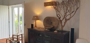 Una habitación con un mueble de madera oscura, una silla de mimbre, una lámpara, una escultura de árbol decorativa y una luminaria de pared.