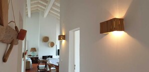 Un pasillo con decoración rústica en la pared, una lámpara de pared de madera y una puerta que da a una habitación con cama y televisor.