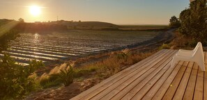 Una terraza de madera con vistas a un campo de cultivos y una colina distante con edificios.