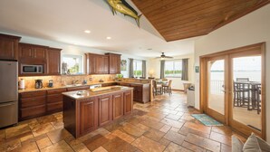 A spacious kitchen with wooden cabinets, a large island, and a view to the outside. - Captains Quarters - Cudjoe Key - Pool- Waterfront w/ Boat Dock (Cudjoe Key)