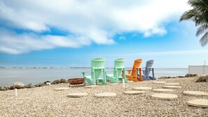 A pebbled beach with three Adirondack chairs in green, orange, and gray. - Captains Quarters - Cudjoe Key - Pool- Waterfront w/ Boat Dock (Cudjoe Key)