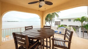 A covered outdoor dining area with a table and chairs, a ceiling fan, and a view of the ocean. - Captains Quarters - Cudjoe Key - Pool- Waterfront w/ Boat Dock (Cudjoe Key)