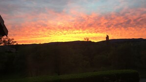 Ein Sonnenuntergang über einer hügeligen Landschaft mit Baum- und Gebäudesilhouetten.