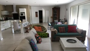 Ein modernes Wohnzimmer mit einer Couch, Sesseln, einem Couchtisch und einem Essbereich, im Hintergrund eine Küche.