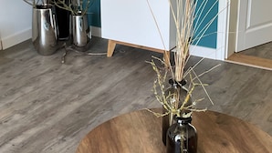 Ein Zimmer mit Holzboden, einem runden Holztisch und drei Blumentöpfen.
