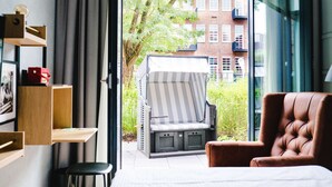Una habitación moderna con un ventanal grande, una silla a rayas, un sillón marrón y una mesita pequeña.
