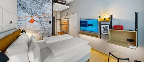 A modern hotel room with a large bed, a TV, a map on the wall, and a small table with a chair.