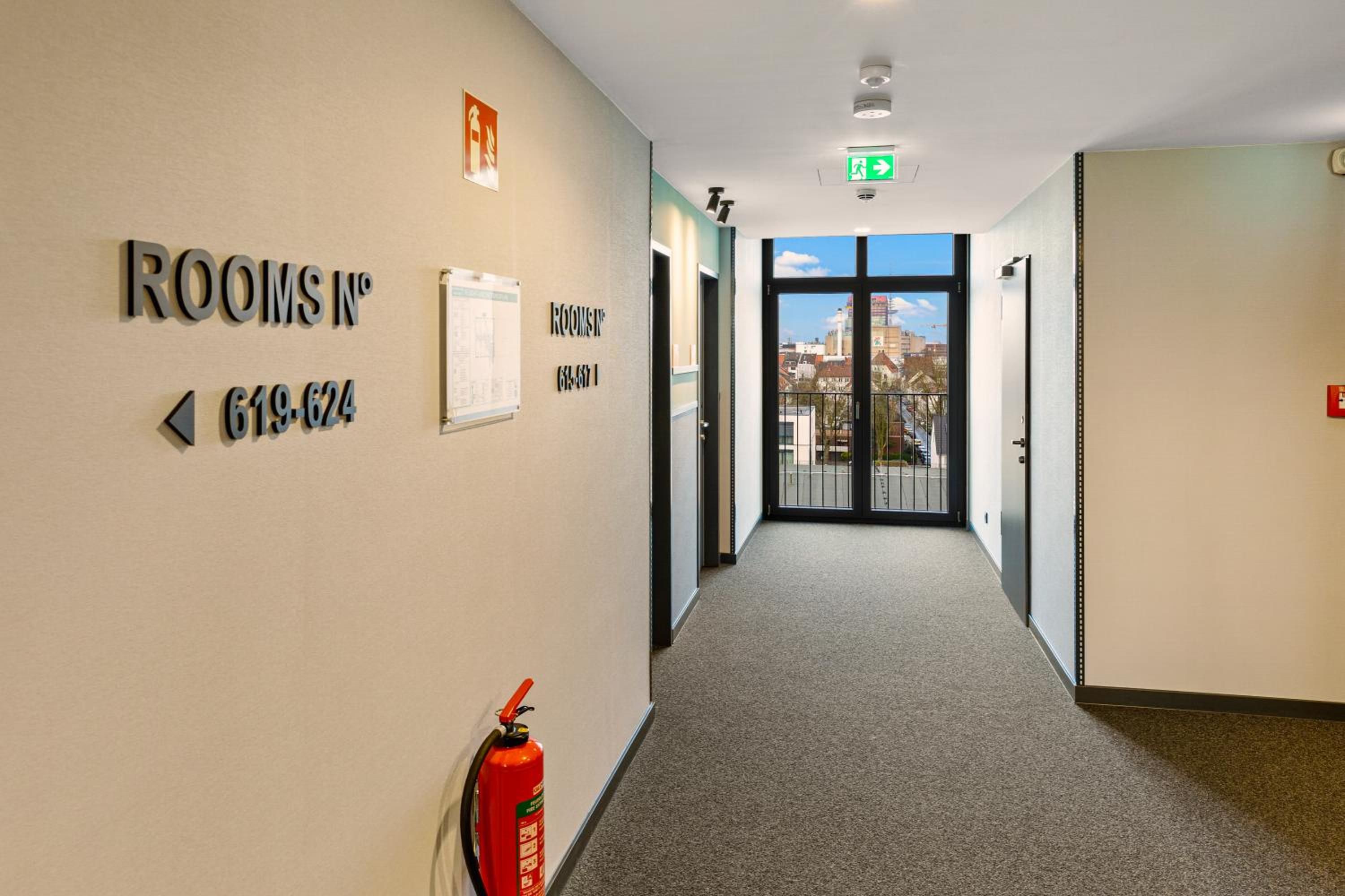 Un pasillo de hotel con carteles indicativos hacia las habitaciones y un extintor.