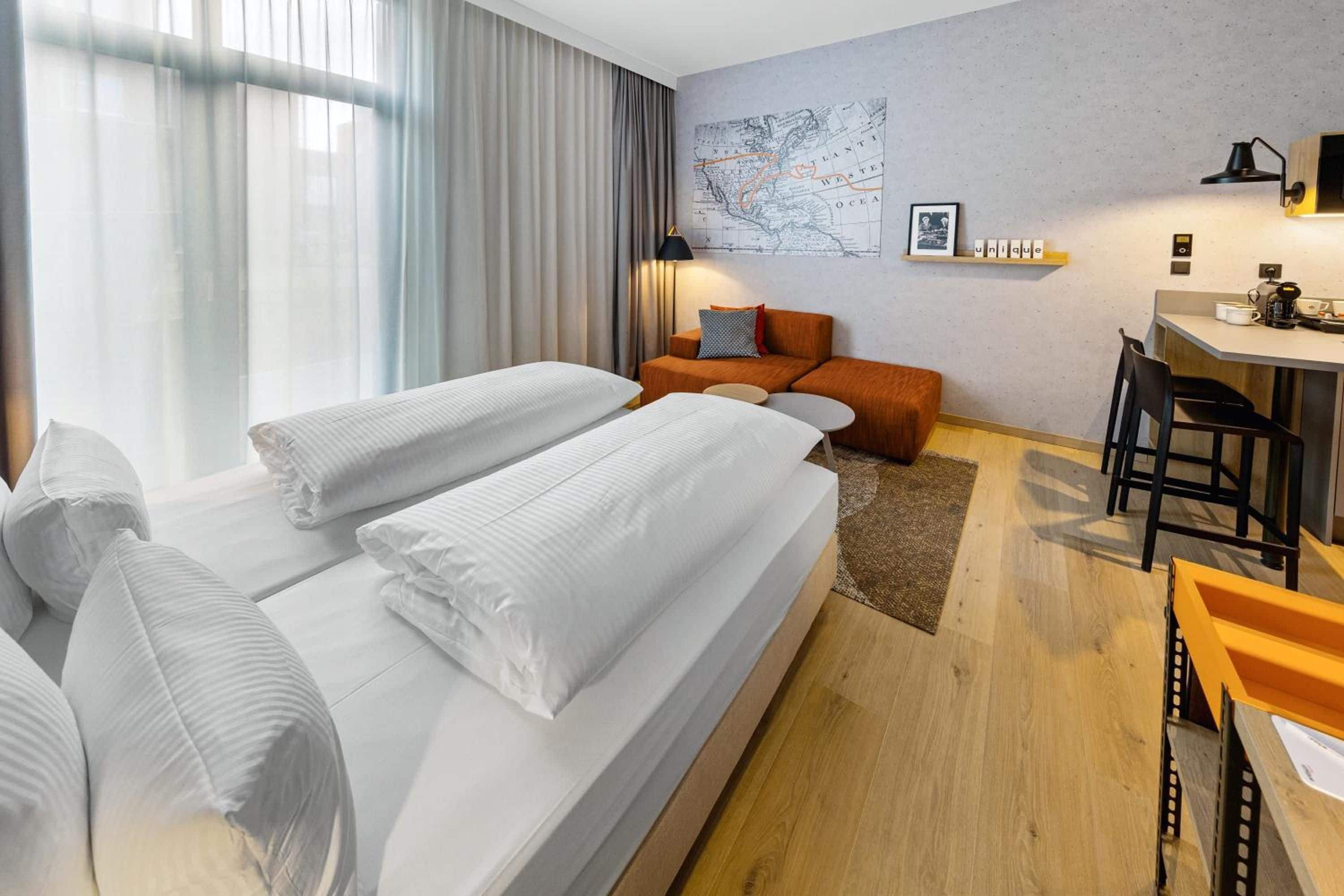 A hotel room with two beds, a desk, a chair, a map on the wall, and a window with curtains.