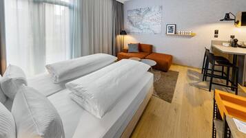 A hotel room with two beds, a desk, a chair, a map on the wall, and a window with curtains.